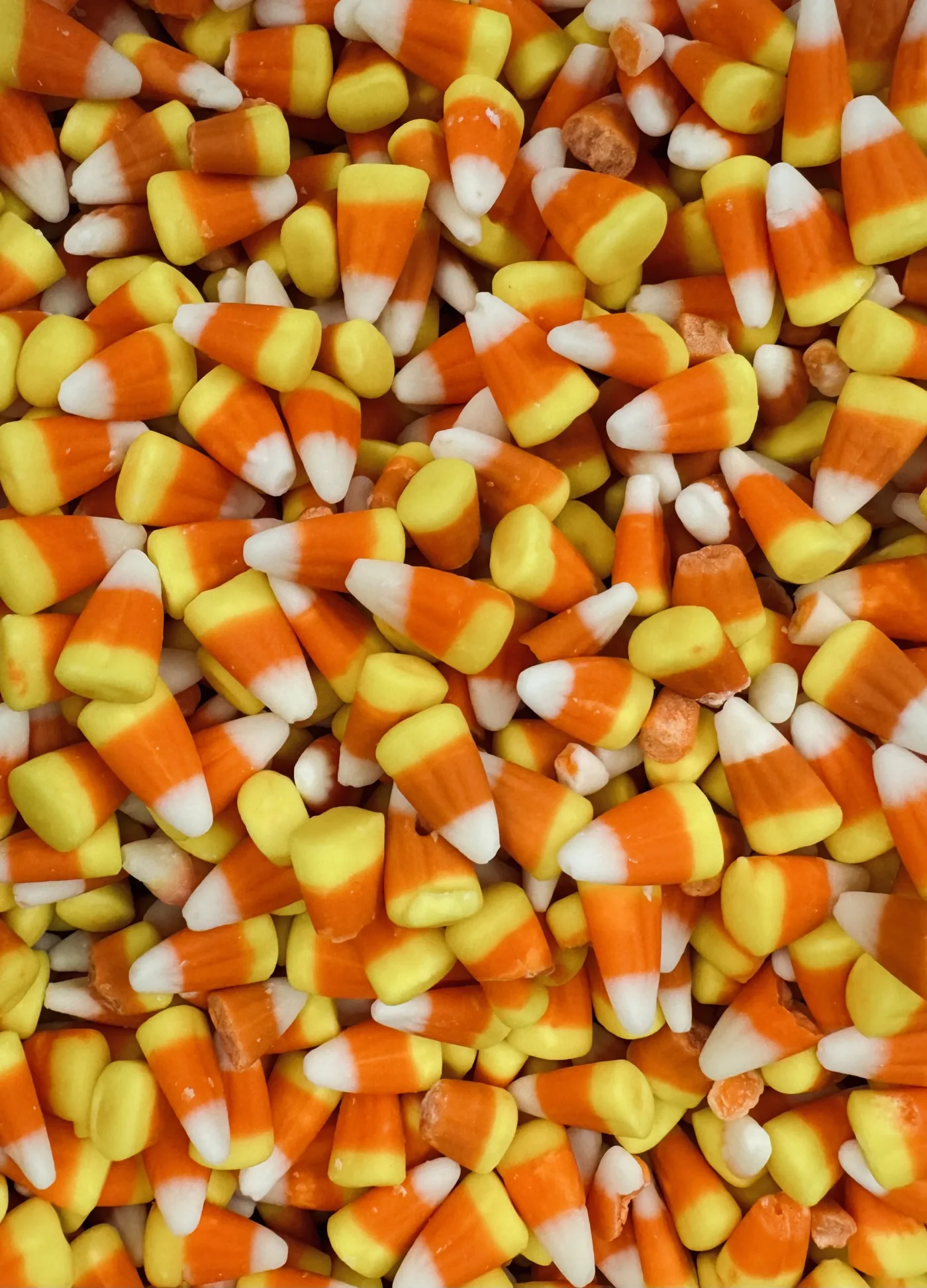 Orange, yellow, and white candy corn pieces in a round orange bowl beside a small pumpkin