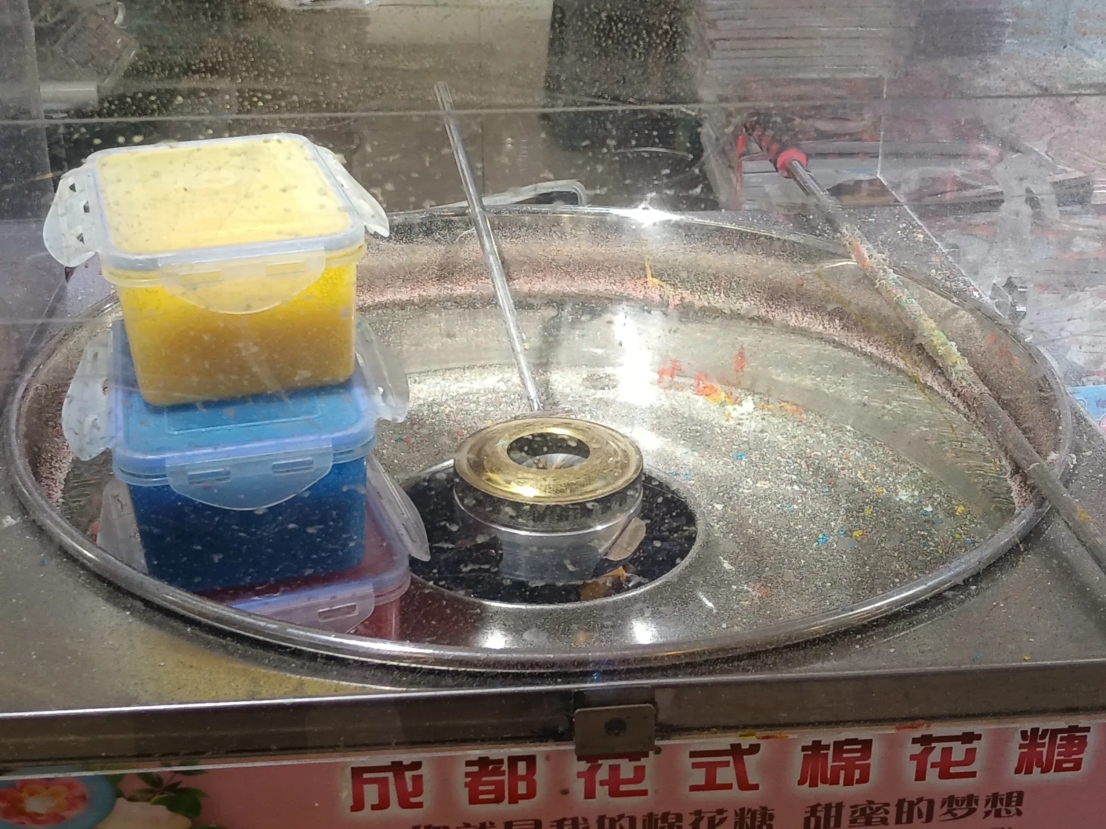 A metal cotton-candy machine with a central spinner, sugar containers, and colorful sugar specks
