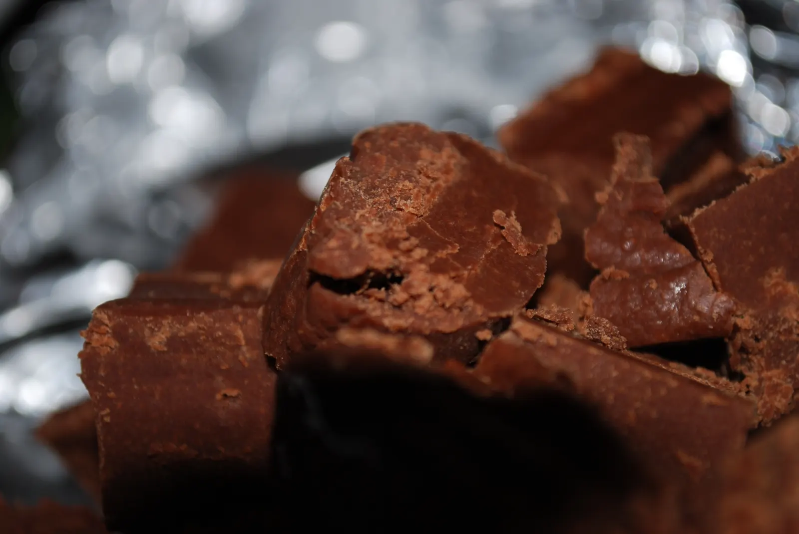 Close view of several uneven squares of chocolate fudge on crinkled foil