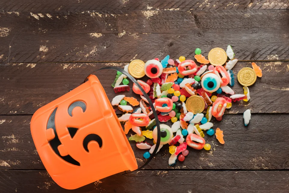 A pumpkin treat bucket spilling colorful Halloween candy