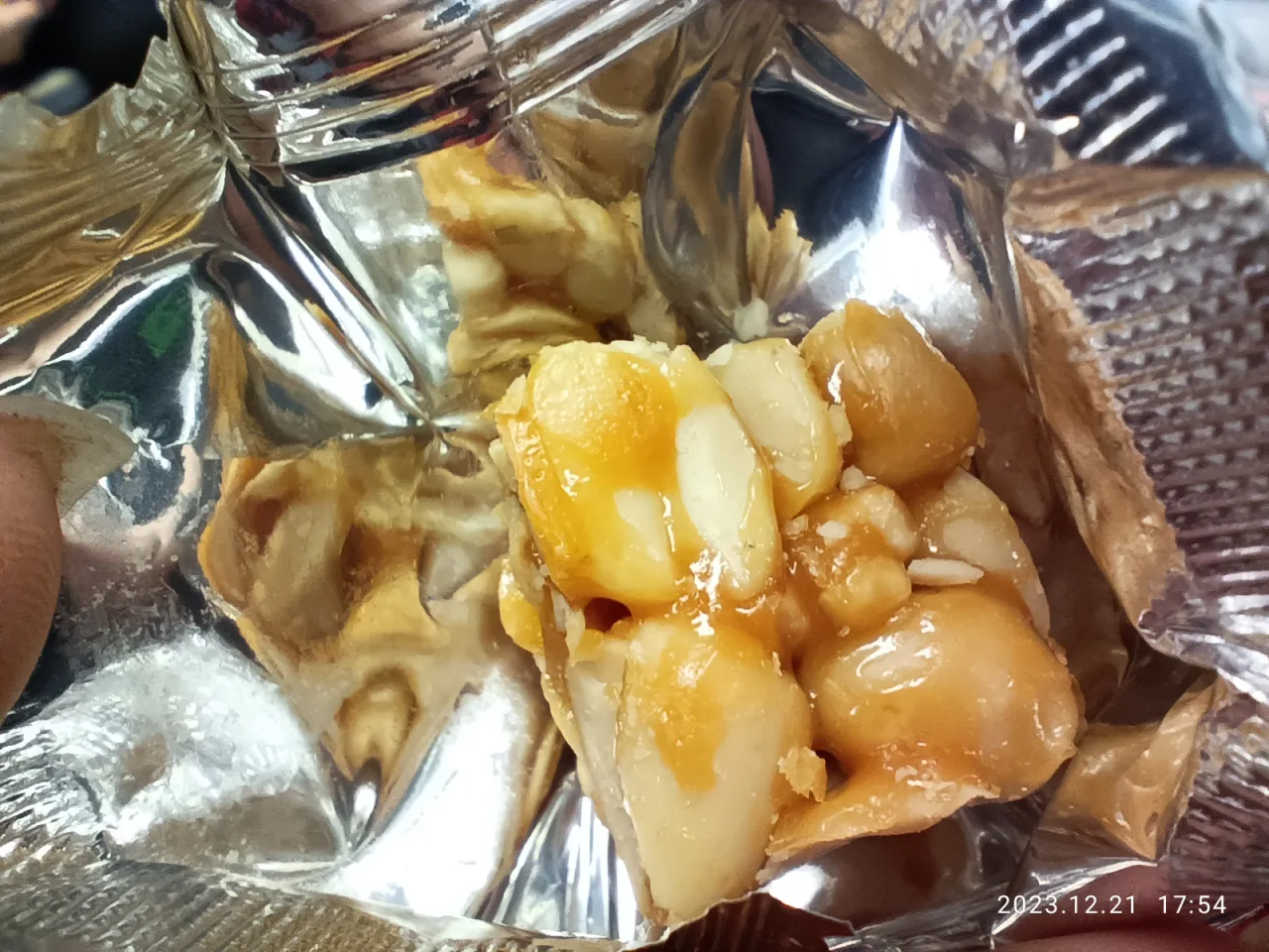 A close view of a broken piece of peanut brittle with whole and split peanuts in a silver wrapper