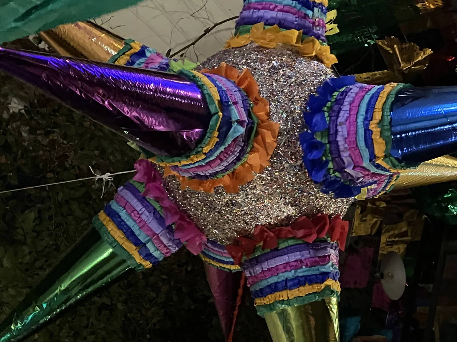 Colorful star-shaped piñata with purple, green, and gold cones hanging outdoors at night