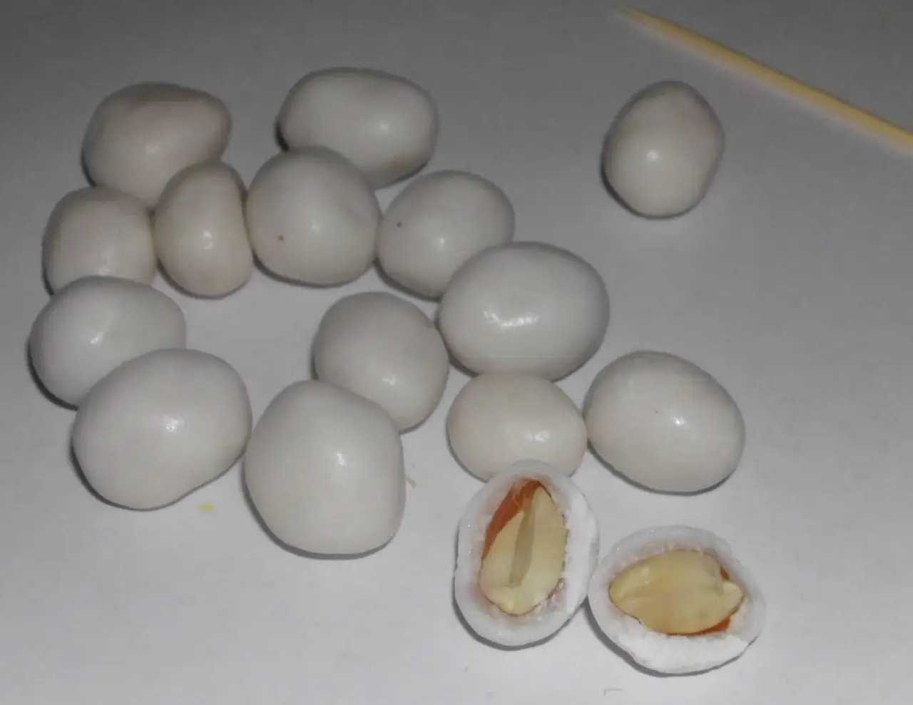 White sugar-coated peanut candies on a plate, with two pieces cut open to reveal peanuts inside
